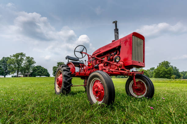 A vintage red tractor on a green farm field and blue sky with cumulus clouds.